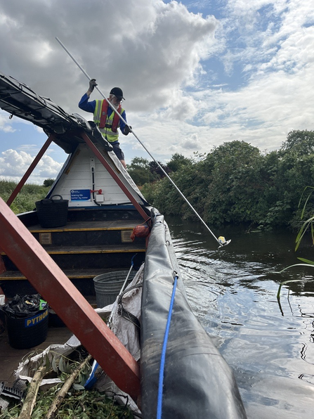 A man litter picking out of a canal boat