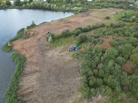 Tractor on land adjacent to water clearing vegetation (scrub)